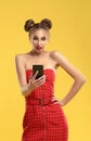 Girl in red dress with hair buns surprised and looking to smartphone on yellow background Royalty Free Stock Photo