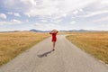 Girl in the red dress and hat walking along the road in the mountains