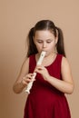 Girl in red dress play melody on flute with concentration, blowing air into duct, beige background. Learn to play