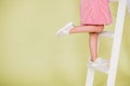 A girl in a red dress poses on the stairs, lifting her leg up and showing off white sneakers. Comfortable children shoes Royalty Free Stock Photo