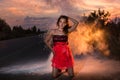 Girl in red dress on the road and white flour cloud behind her in the evening at sunset Royalty Free Stock Photo