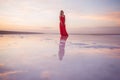 A girl in a red dress stands in the water of a mirror lake at sunset. Reflection of a girl and clouds at sunset Royalty Free Stock Photo