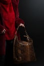 Girl in a red fur coat holds a brown leather bag on black background, brown leather ladies handbag hanging on the brush in the gir Royalty Free Stock Photo