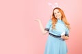 A girl with red hair in a blue dress and easter bunny ears on a pink background. A beautiful woman is pointing at a product or Royalty Free Stock Photo