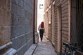 Girl with red hair in dress passing trough city tiny shallow street passage