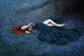 Girl with red hair lying on grass in dark forest, black queen lost in battle, charming lady in long black royal dress Royalty Free Stock Photo