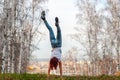 A girl with red hair stands on her hands with her back to the camera on a hill against the background of a blurred birch forest. Royalty Free Stock Photo