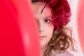 Girl in a red hat hiding behind a red balloon