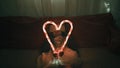 Girl in red hat holding big luminous heart formed with two candy sticks over dark background