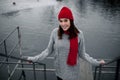 Girl in red hat and scarf walking in winter park near lake. Royalty Free Stock Photo
