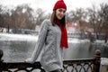 Girl in red hat and scarf walking in winter park near lake. Royalty Free Stock Photo