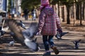 Girl in a red jacket, hat and glasses chasing pigeons in the park. Royalty Free Stock Photo