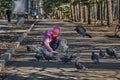 Girl in a red jacket, hat and glasses chasing pigeons in the park. Royalty Free Stock Photo