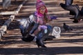 Girl in a red jacket, hat and glasses chasing pigeons in the park. Royalty Free Stock Photo