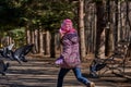 Girl in a red jacket, hat and glasses chasing pigeons in the park. Royalty Free Stock Photo