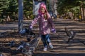 Girl in a red jacket, hat and glasses chasing pigeons in the park. Royalty Free Stock Photo