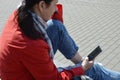 A girl in a red jacket holds a smartphone in her hands on the street, sitting in a city park. Online learning, correspondence in Royalty Free Stock Photo