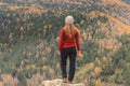 A girl in a red jacket looks out into the distance on a mountain, a view of the mountains and an autumnal forest by an overcast da