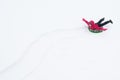 Girl in a red jacket riding an inflatable pillow in the snow leaving traces