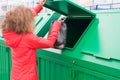 Girl in a red jacket, throws a full package in a green dumpster, close-up