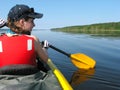 Girl in a red life jacket rows in a kayak on a lake on a sunny s