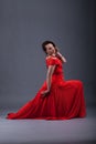 Girl in a red long dress in the studio, on a gray background. The dress is wearing a red leather sword belt.