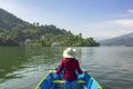 Girl in a red shirt and hat in a wooden blue boat on the lake on the background of green mountains Royalty Free Stock Photo