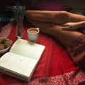 Girl in a red shirt on a plaid reading a book over a cup of coffee