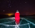 girl in red sits on an ice-lit frozen Lake Baikal under a starry night sky with the constellation Orion, Siberia, Russia Royalty Free Stock Photo