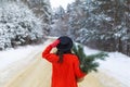 A girl in a red sweater and hat, red mittens stands in the middle of a snow-covered road in a forest with pine branches. Weekend Royalty Free Stock Photo