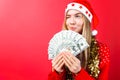 A girl in a red sweater and a Santa hat, holds the money and looks away thinking where to spend it on a red background Royalty Free Stock Photo