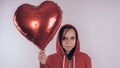 A girl in a red sweatshirt in her hand a red balloon in the form of a heart. Student posing on white background