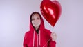 A girl in a red sweatshirt in her hand a red balloon in the form of a heart. Student posing on white background