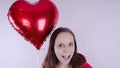 A girl in a red sweatshirt in her hand a red balloon in the form of a heart. Student posing on white background