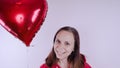 A girl in a red sweatshirt in her hand a red balloon in the form of a heart. Student posing on white background