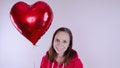 A girl in a red sweatshirt in her hand a red balloon in the form of a heart. Student posing on white background