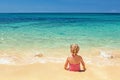 Girl in red swimsuit sitting on the sand beach edge