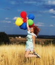 Girl redhead jumping with ballons at the yellow spikelets and blue sky Royalty Free Stock Photo