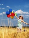Girl redhead jumping with ballons at the yellow spikelets and blue sky