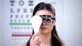 Girl in refractor closing one eye, ophthalmologist appointment, vision check-up Royalty Free Stock Photo