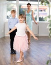 Girl rehearsing elegant curtsy with boy dance partner and female teacher