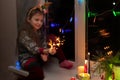 a girl with reindeer horns sits on a window with sparklers at Christmas. near candles and garlands Royalty Free Stock Photo