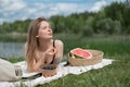 Girl relaxing and eat watermelon outdoor near lake. Picnic in nature