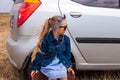 Girl relaxing and enjoying road trip sitting by the silver car. Happy child rides toward adventure. Lady in denim jacket Royalty Free Stock Photo