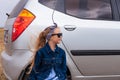 Girl relaxing and enjoying road trip sitting by the silver car. Happy child rides toward adventure. Lady in denim jacket Royalty Free Stock Photo