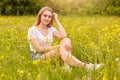 Girl relaxing in meadow, blonde beautiful young woman sitting on grass surrounded with field flowers and enjoying summer day, Royalty Free Stock Photo