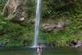 Girl in remote freshwater lagoon under waterfall