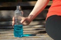 Girl is resting on a park bench holding a blue isotonic drink in her hand