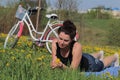 The girl is resting on the spring meadow. Lies on the bedspread. Nearby is a bike. Dandelions are blooming, young grass is growing Royalty Free Stock Photo