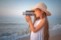 Girl with a retro vintage camera taking photos and film of a beautiful sea sunrise and beach Royalty Free Stock Photo